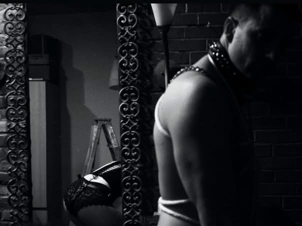 A cropped figure wearing studded leather beside an ornate mirror in a dark black-and-white interior